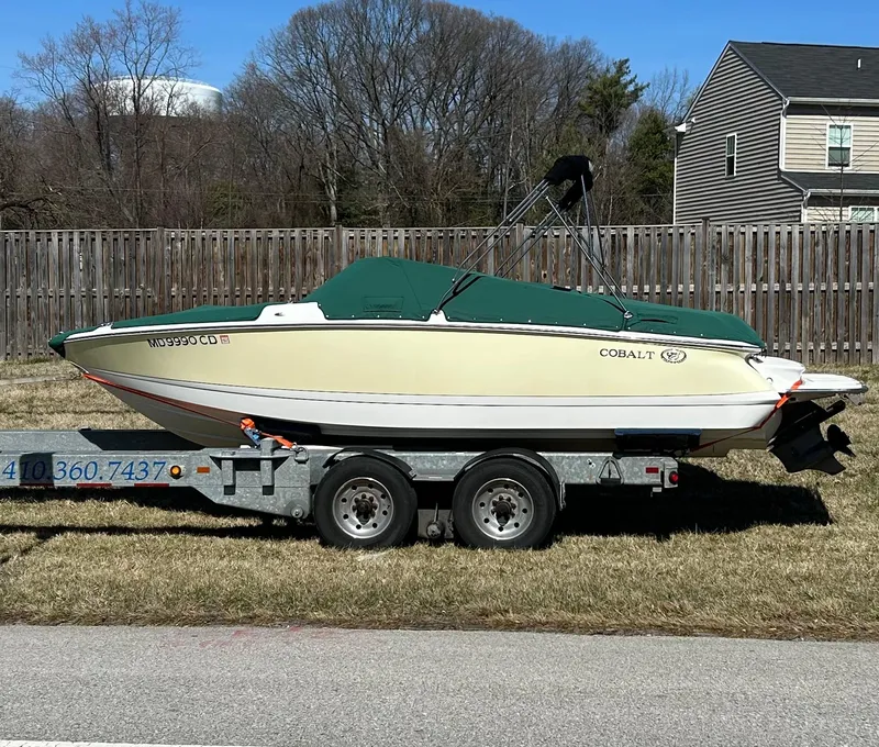 The Image of 2012 Cobalt 210 WSS boat on trailer, green cover, parked on grass. - 0