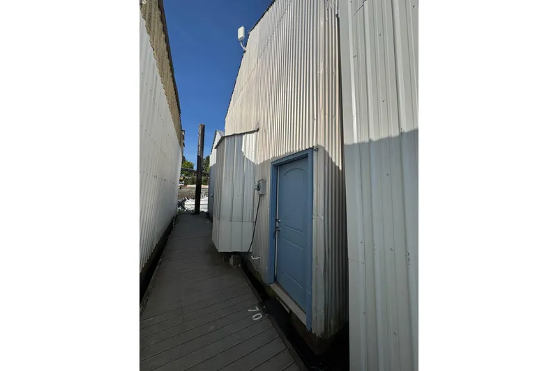 Slide: The Image of Narrow walkway between custom boathouse structures, featuring blue door and corrugated metal walls. - 2