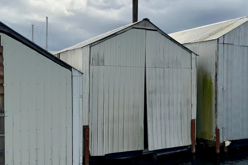 Slide: The Image of Custom 2000 boathouse with white metal siding, docked on a cloudy day. - 5