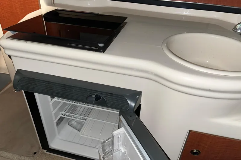 Slide: The Image of 2004 Sea Ray Sundancer 260 kitchenette with sink, stove, and open mini fridge. - 26