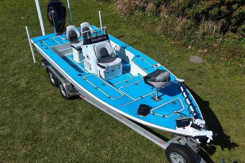 Slide: The Image of 2023 ShearWater X22 Hybrid boat on trailer, blue deck, parked on grass. - 22