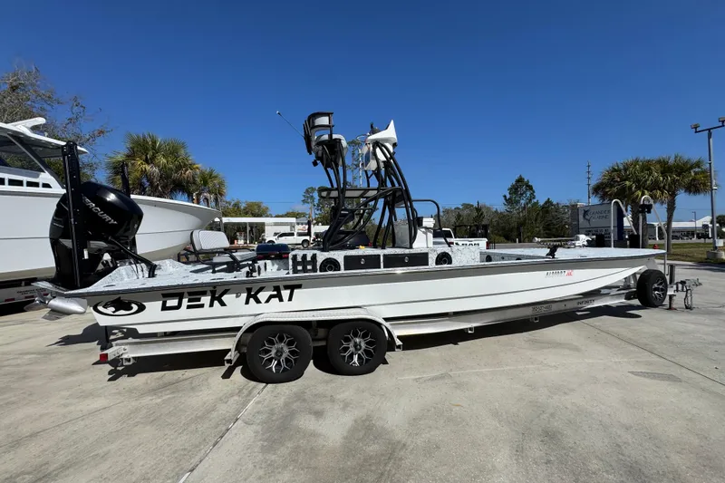 Slide: The Image of 2023 Dek Kat 27 Trilogy boat on trailer, parked outdoors under clear blue sky. - 9