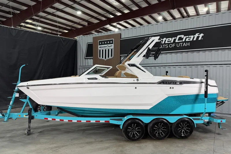 Slide: The Image of 2025 MasterCraft XStar 23 boat in showroom, white and turquoise design, on trailer. - 2