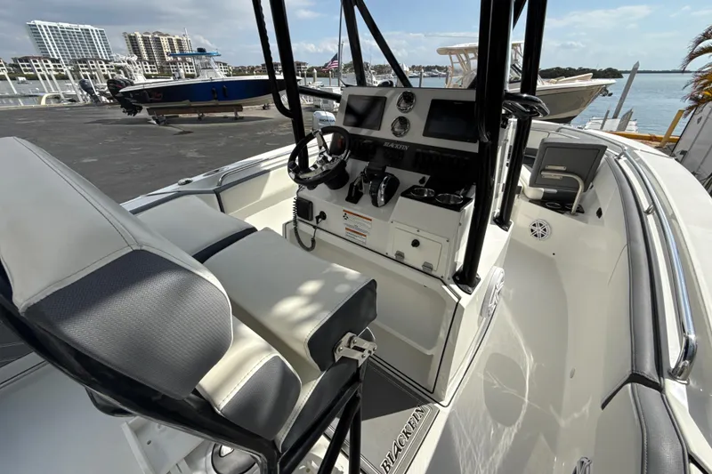 Slide: The Image of 2018 Blackfin 212 CC boat interior with steering console and seating, docked near waterfront. - 2