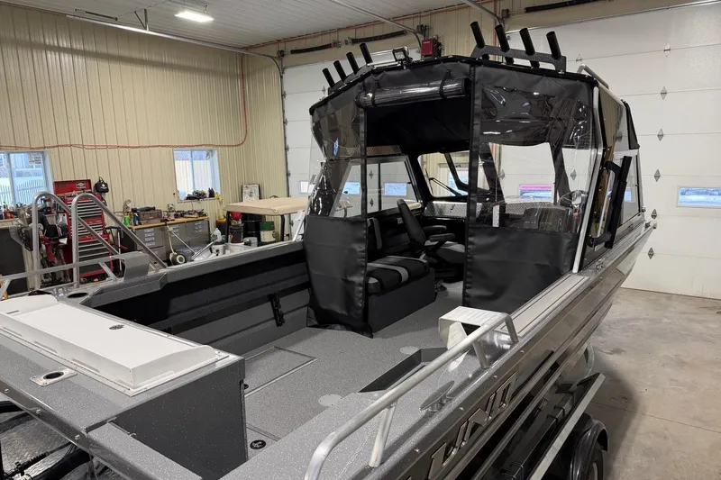 Slide: The Image of 2026 Lund 210 Heavy Gauge boat in a garage, showcasing interior seating and fishing rod holders. - 18