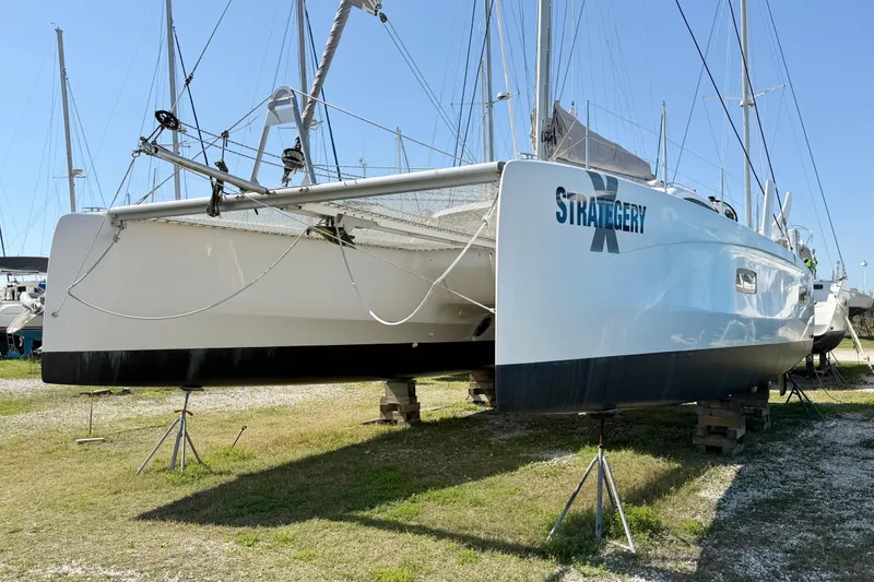 Slide: The Image of 2014 Outremer 45 catamaran on land, named "Strategery X," under clear blue sky. - 94