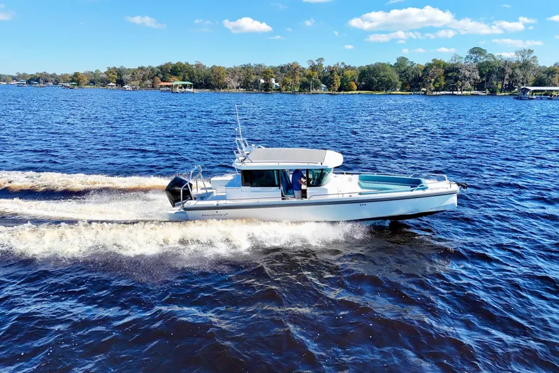 Slide: The Image of 2020 Axopar 28 CABIN boat cruising on a sunny lake with scenic shoreline. - 1