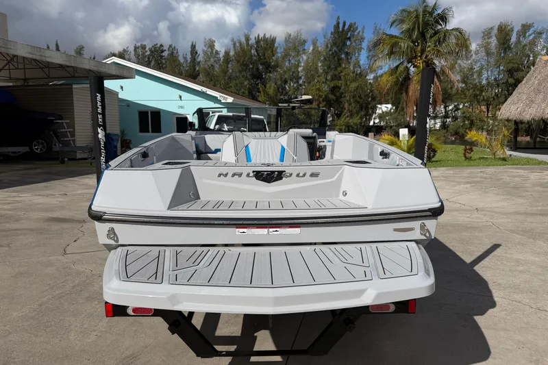 Slide: The Image of 2026 Nautique Ski Nautique boat, rear view, parked outdoors under a sunny sky. - 11