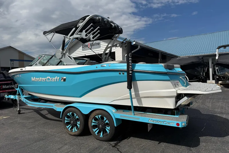 Slide: The Image of 2017 MasterCraft XT23 boat in blue and white on a matching trailer, parked outside a marine shop. - 1