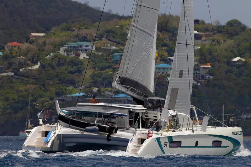 Slide: The Image of 2020 Outremer 51 catamaran sailing near a lush, hilly coastline. - 1