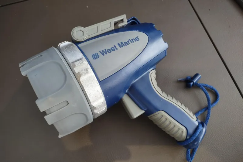 Slide: The Image of Blue and gray West Marine spotlight with a wrist strap on a brown surface. - 161