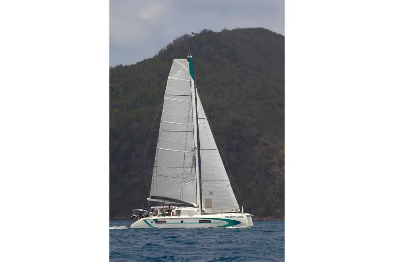 Slide: The Image of 2020 Outremer 51 catamaran sailing near a lush, mountainous coastline. - 4