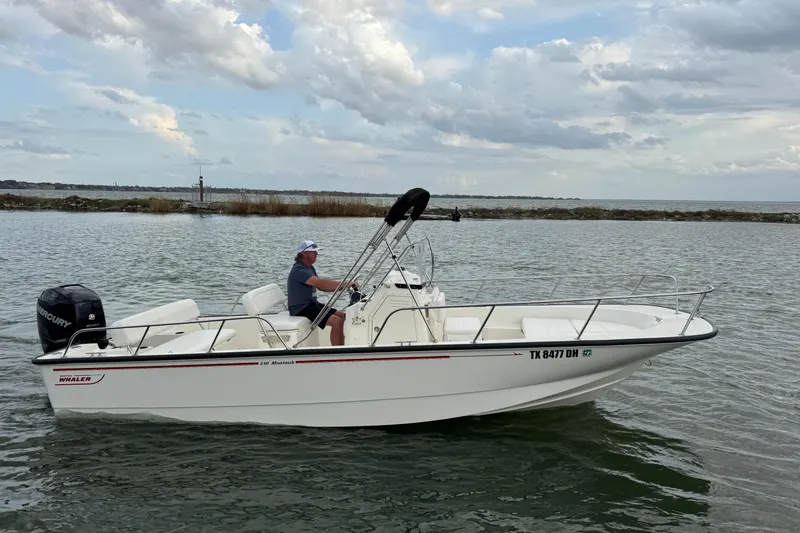 Slide: The Image of 2016 Boston Whaler 210 Montauk boat on water, with person steering under cloudy sky. - 5