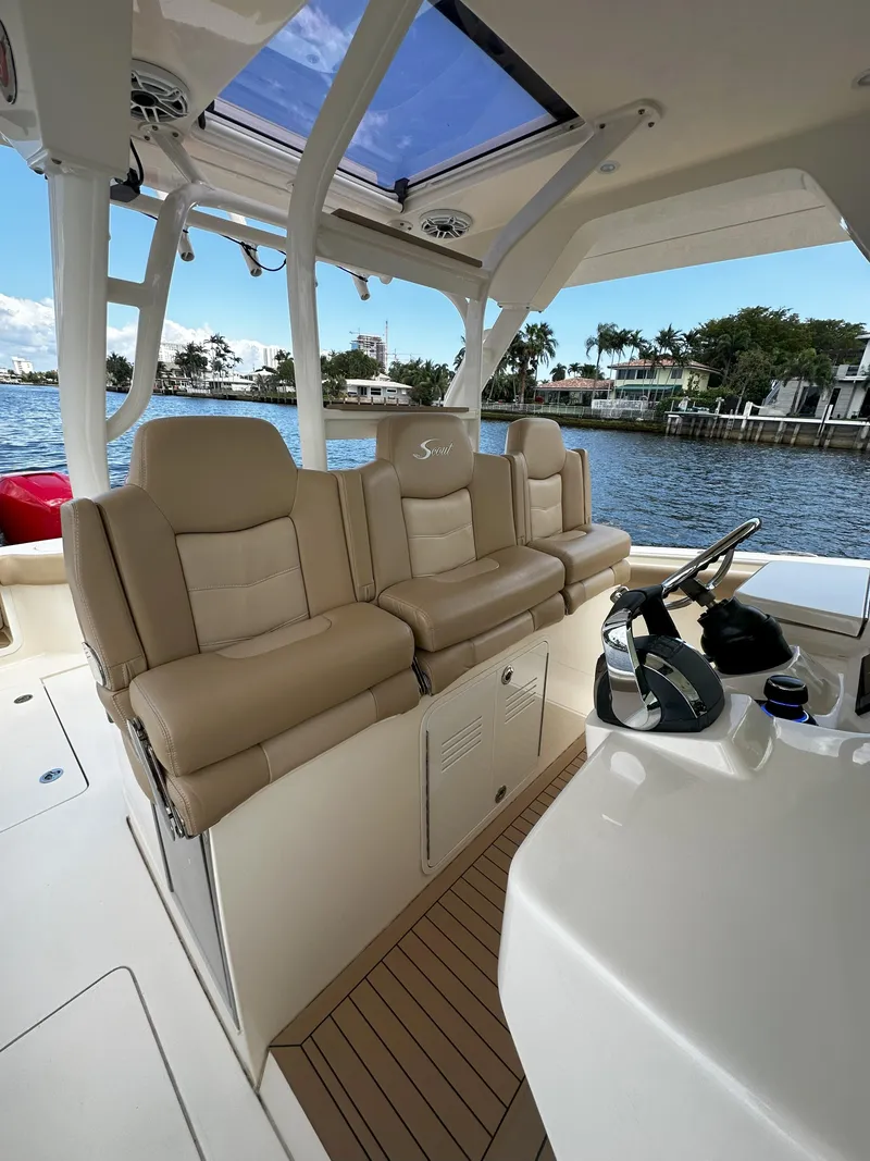 Slide: The Image of 2020 Scout 380 LXF boat interior with beige seating and helm, docked by waterfront homes. - 14