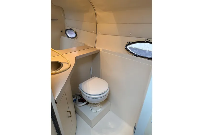 Slide: The Image of 1997 Larson Cabrio 310 Mid-Cabin bathroom with sink and toilet, featuring porthole windows. - 16