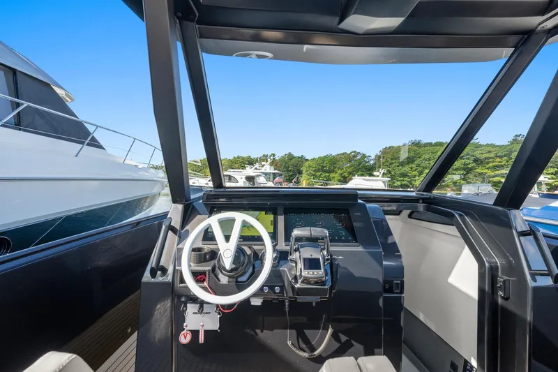 Slide: The Image of 2024 Vanquish Yachts 40 helm with modern controls and steering wheel, docked near other boats. - 52