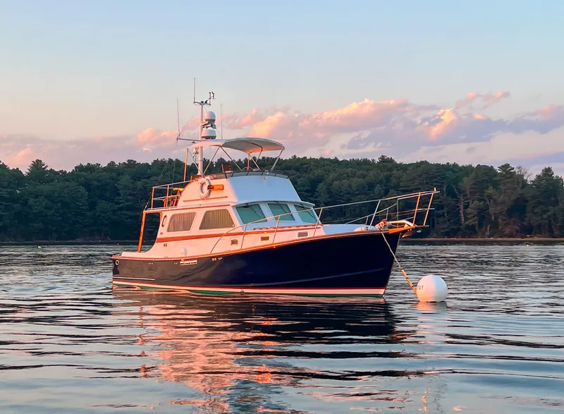Slide: The Image of 1984 Wilbur 38 boat anchored on calm water at sunset, surrounded by trees. - 2
