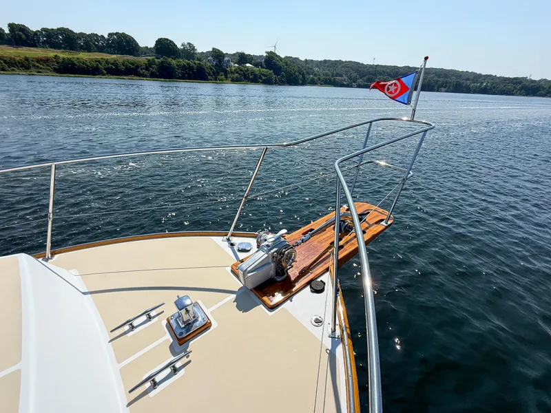 Slide: The Image of Bow of 1984 Wilbur 38 boat with flag, cruising on a calm lake. - 47