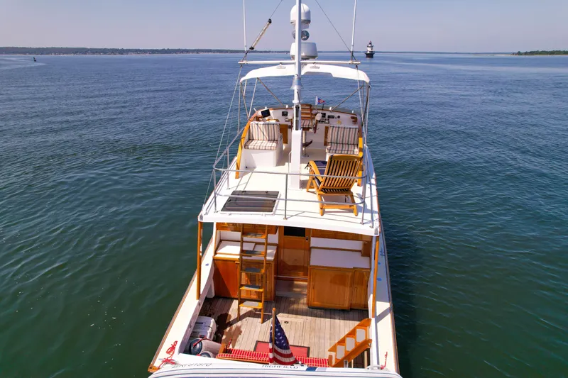Slide: The Image of 1984 Wilbur 38 yacht on calm water, featuring wooden deck chairs and American flag. - 49