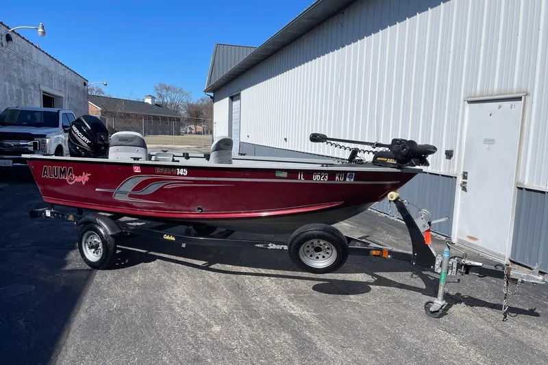 The Image of 2016 Alumacraft Escape 145 Tiller boat on trailer, parked outside a building. - 0