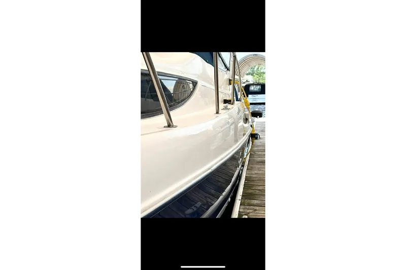 Slide: The Image of 2005 Bayliner 305 boat side view at dock, showcasing sleek design and railing. - 13