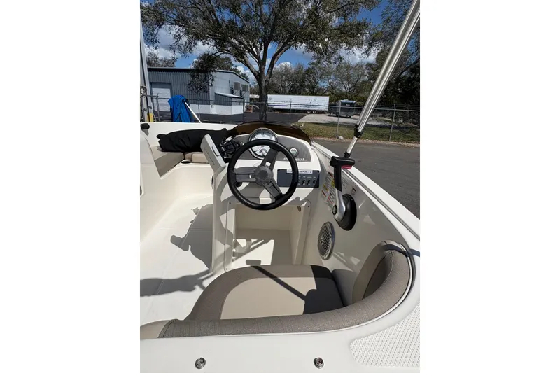 Slide: The Image of 2016 Bayliner 160 Bowrider interior with steering wheel and seating, parked outdoors. - 5