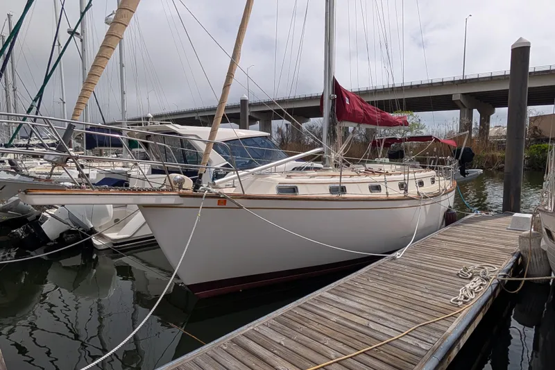 Slide: The Image of 1988 Island Packet 38 sailboat docked at marina with red sails and wooden deck. - 45