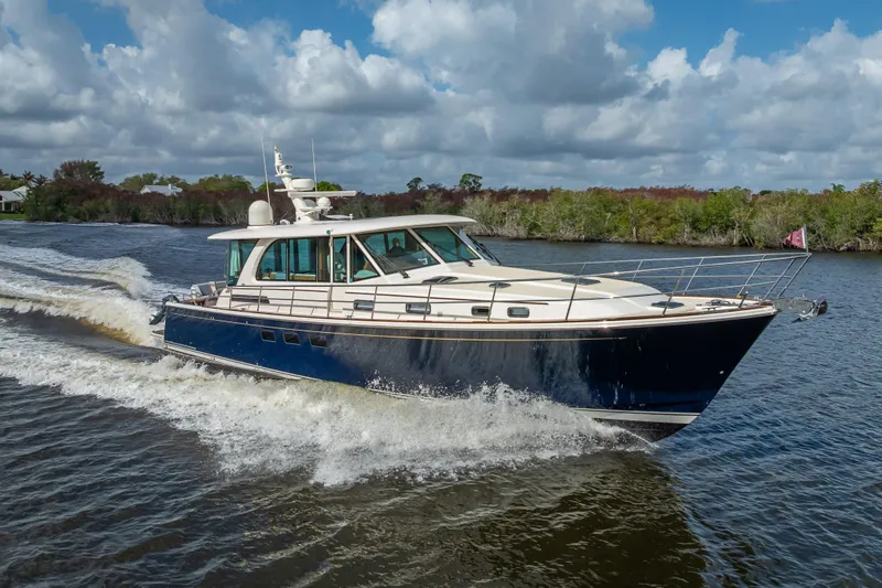 Slide: The Image of 2025 Sabre 58 Salon Express yacht cruising on a scenic river under a cloudy sky. - 7