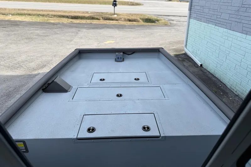 Slide: The Image of 2026 SeaArk 2472 CUB boat deck with storage compartments, parked near a building. - 10