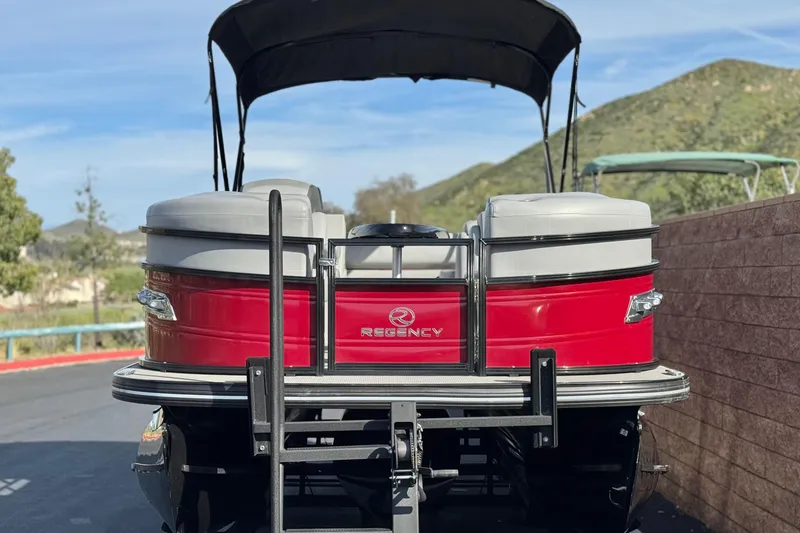 Slide: The Image of 2023 Regency 250 DL3 pontoon boat, red exterior, parked with scenic mountain backdrop. - 2