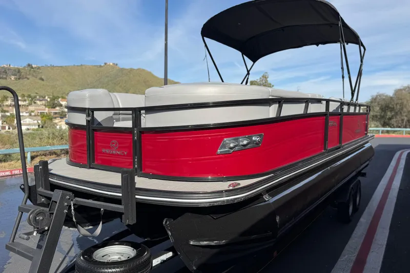 Slide: The Image of 2023 Regency 250 DL3 pontoon boat with red exterior and canopy, parked on a trailer. - 3