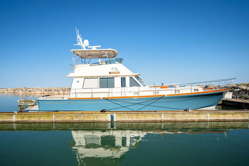 The Image of 2004 Grand Banks 58 Eastbay FB yacht docked on calm water under clear blue sky. - 0