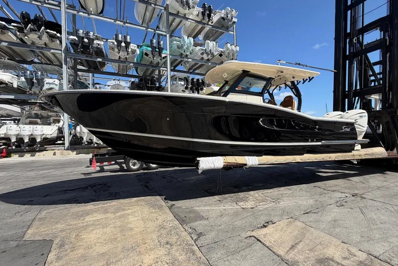 The Image of 2021 Scout 330 LXF boat in storage, black hull, sunny day, marina background. - 0