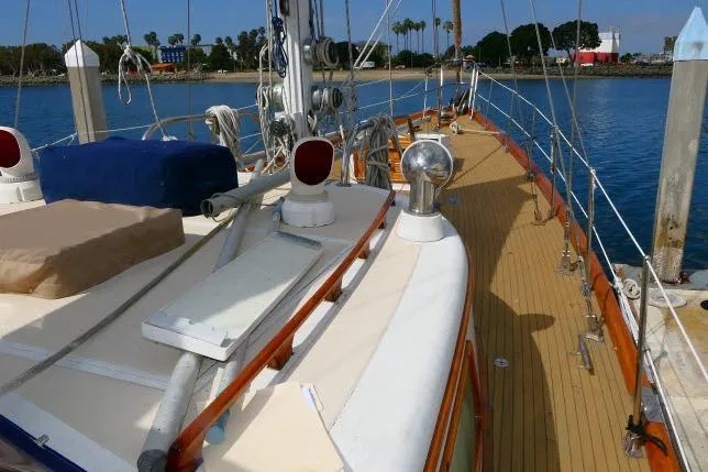 Slide: The Image of 1982 Ta Shing Mason 63 sailboat deck with wooden accents, docked by a calm shoreline. - 80