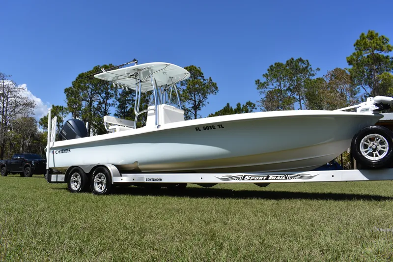 Slide: The Image of 2018 Contender 25 Bay boat on trailer, parked on grass under clear blue sky. - 1