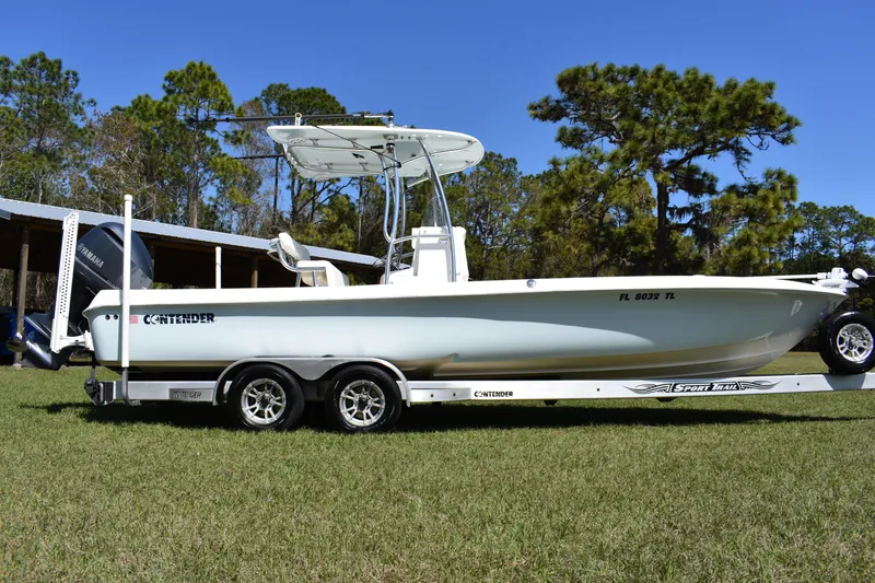 Slide: The Image of 2018 Contender 25 Bay boat on trailer, parked on grass with trees in background. - 2