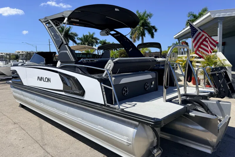 Slide: The Image of 2026 Avalon 2585 Excalibur LTD Tri Toon boat with American flag, parked outdoors. - 10