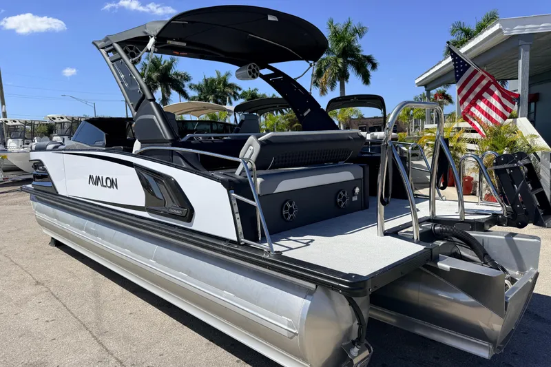 Slide: The Image of 2026 Avalon 2585 Excalibur LTD Tri Toon boat with American flag, parked outdoors. - 9