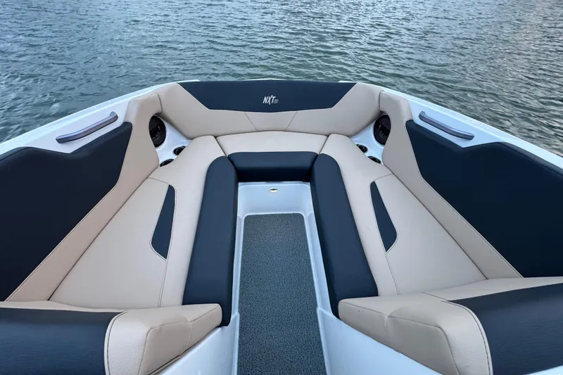 Slide: The Image of 2023 MasterCraft NXT22 boat interior with beige and black seating, on water. - 10