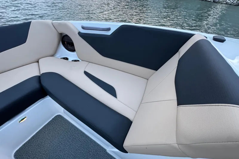 Slide: The Image of 2023 MasterCraft NXT22 boat interior with beige and black seating by the water. - 12