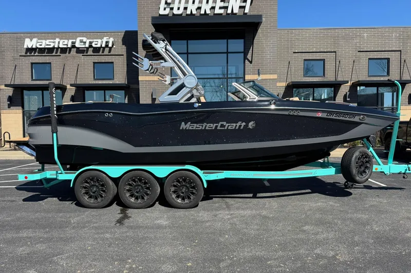 Slide: The Image of 2022 MasterCraft X24 boat on a teal trailer, parked outside a MasterCraft dealership. - 2