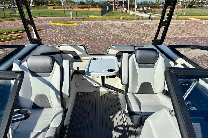 Slide: The Image of 2016 Yamaha Boats AR240 HO interior with seating and table, parked on brick pavement. - 15