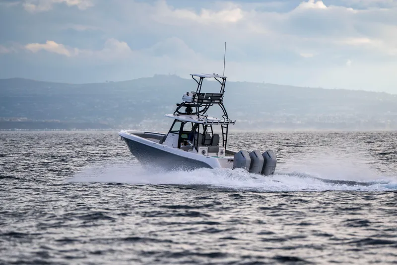 Slide: The Image of 2024 Everglades 365 Center Console boat cruising on open water with scenic backdrop. - 66