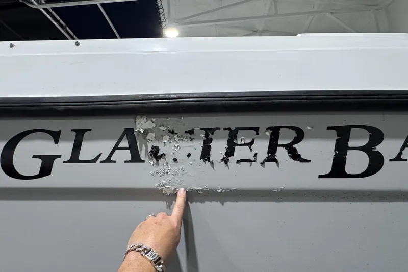 Slide: The Image of Damaged lettering on 2003 Glacier Bay 2640SX Renegade boat hull, with finger pointing. - 12