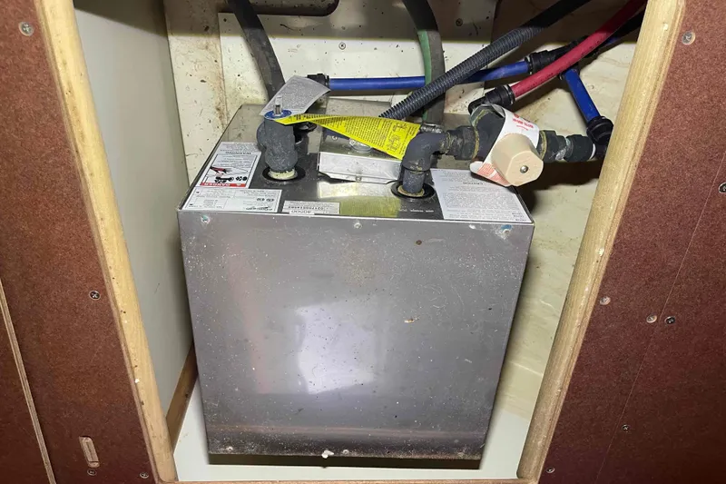 Slide: The Image of 2006 Hunter 36 boat water heater with connected pipes in a wooden compartment. - 16