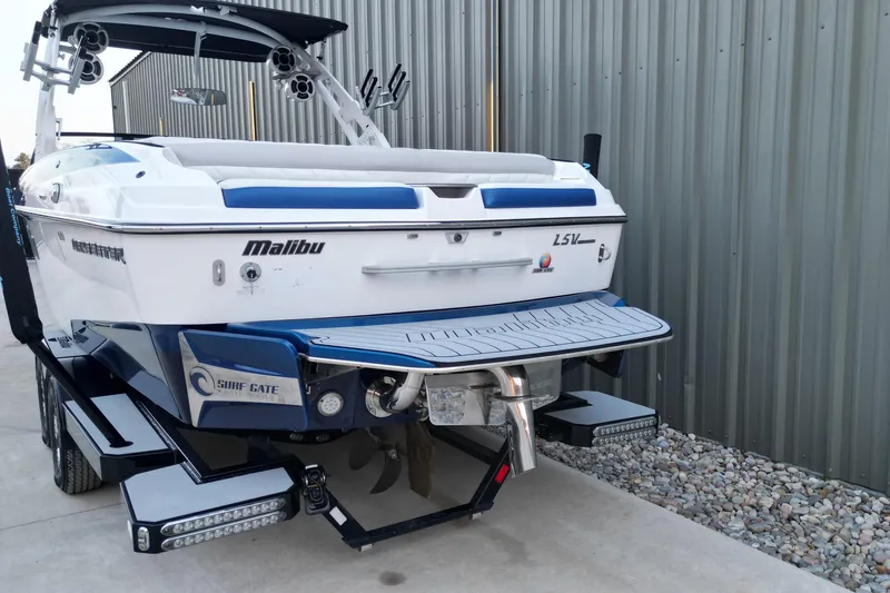 Slide: The Image of 2017 Malibu Wakesetter 25 LSV boat, rear view, parked on a trailer near a metal building. - 14