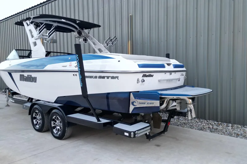 Slide: The Image of 2017 Malibu Wakesetter 25 LSV boat on trailer, parked near a metal building. - 15