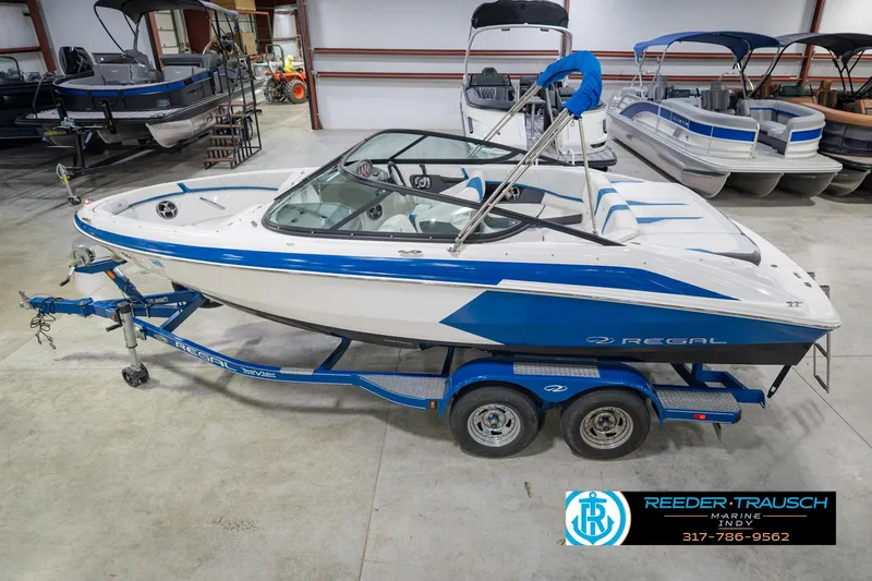 The Image of 2015 Regal 2000 ESX Bowrider boat on trailer in showroom, blue and white design. - 2