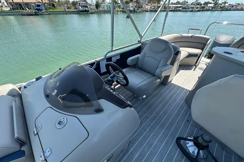 Slide: The Image of 2015 Berkshire 250E Premium pontoon boat interior with helm and seating, docked on calm water. - 13