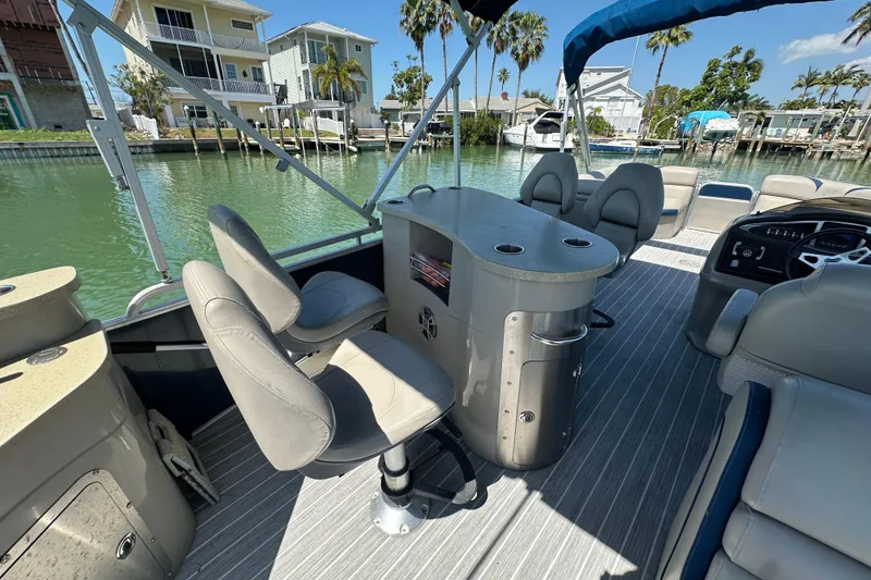 Slide: The Image of 2015 Berkshire 250E Premium pontoon boat interior with seating and helm, docked by waterfront homes. - 18